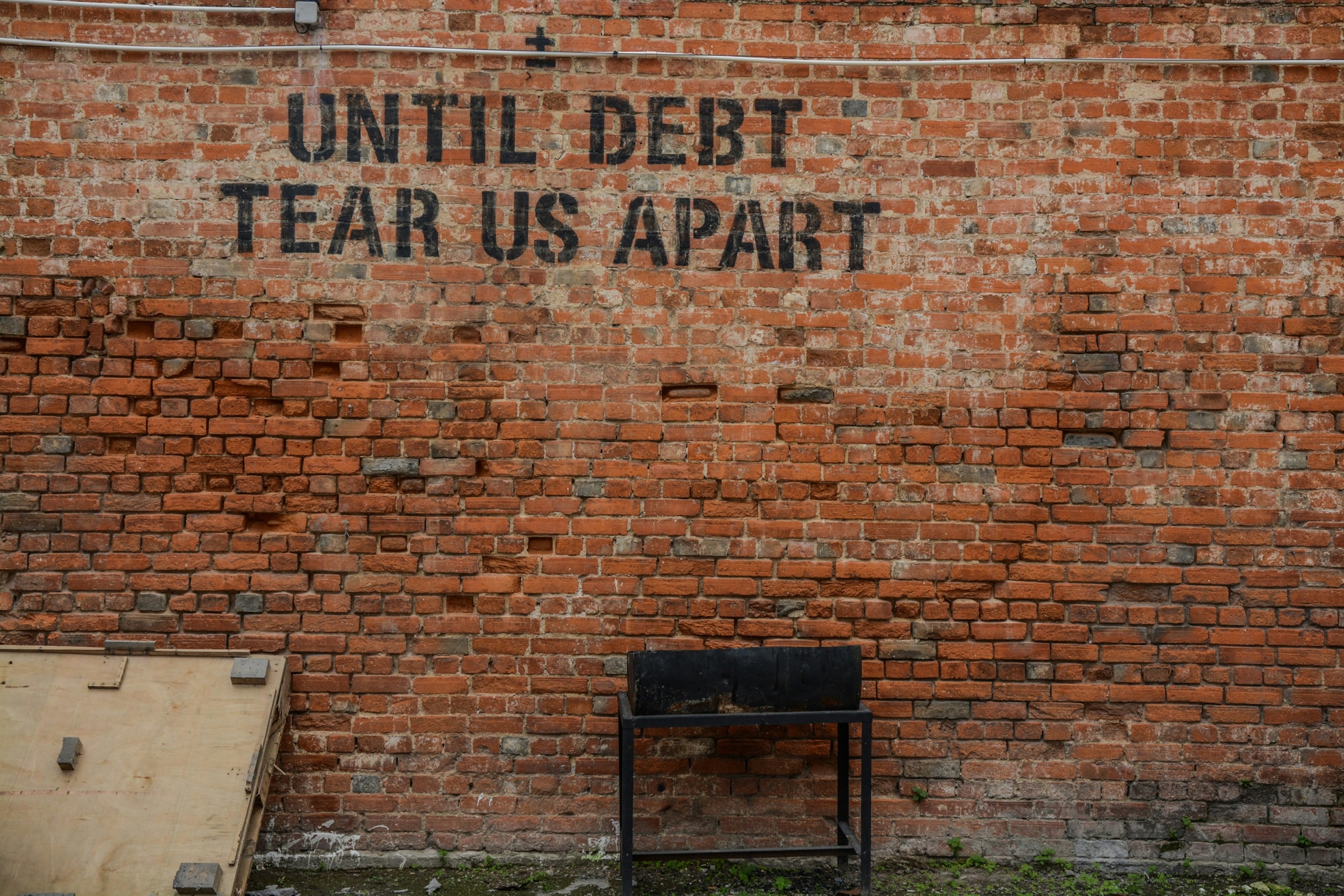 Until debt tear us apart printed red brick wall at daytime